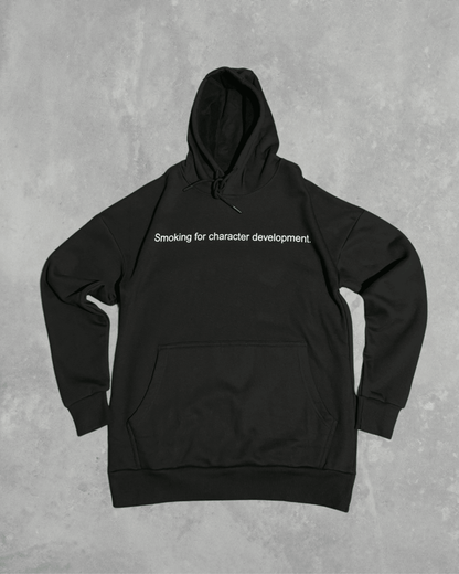 Black heavyweight hoodie with front text 'Smoking for character development' – 400 GSM thick premium streetwear hoodie for men and women.