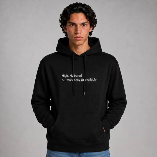 A close up shot of a person wearing a black thick hoodie with text 'High, hydrated & Emotionally Unavailable' with 400 GSM premium streetwear hoodie for men and women and blue jeans on a gray background.