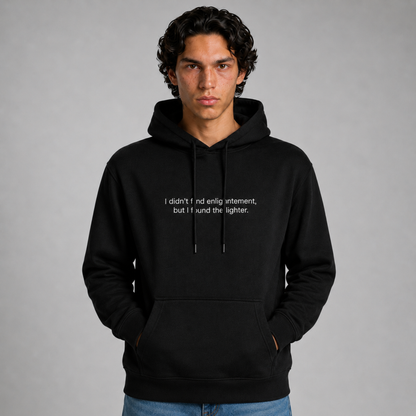 A close up shot of a person wearing a black thick hoodie with text 'I didn't find enlightenment, but I found the lighter' with 400 GSM premium streetwear hoodie for men and women and blue jeans on a gray background.
