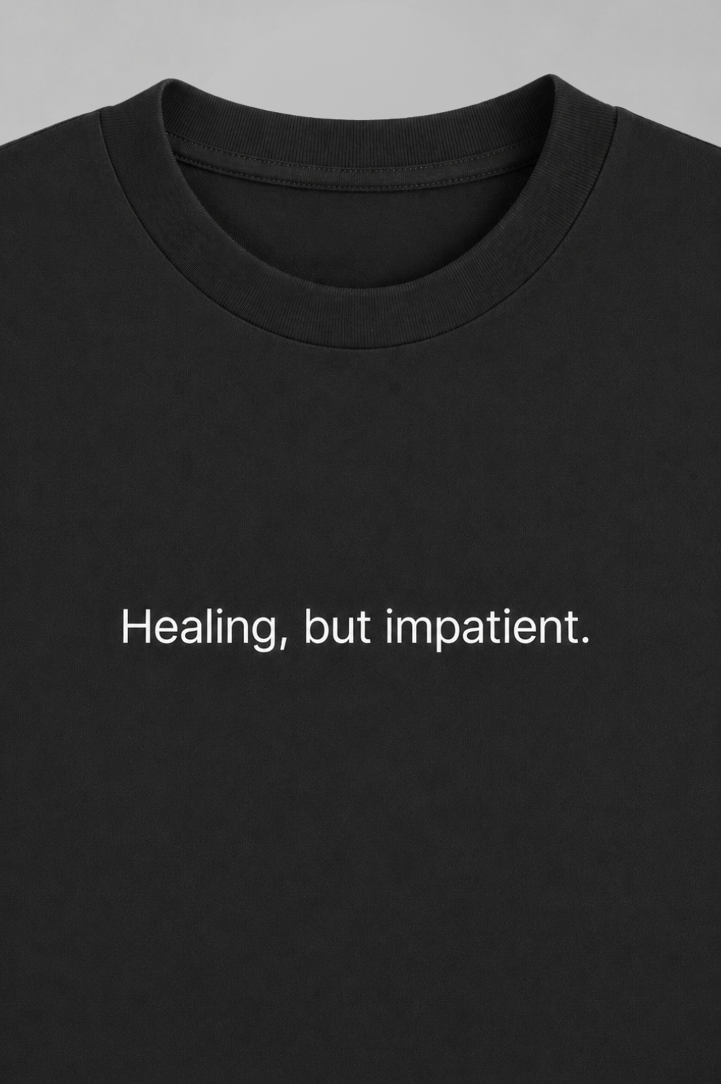 Black t-shirt with white text 'Healing, but impatient.' on a gray background