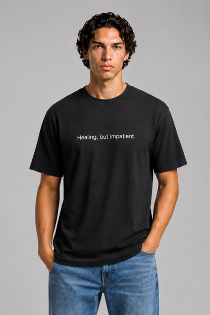 A close up shot of a person wearing a black t-shirt with text 'Healing, but impatient' with 240 GSM premium streetwear t-shirt for men and women and blue jeans on a gray background.