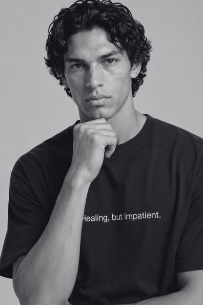 A close up shot of a person wearing a black t-shirt with text 'Healing, but impatient' with 240 GSM premium streetwear t-shirt for men and women.