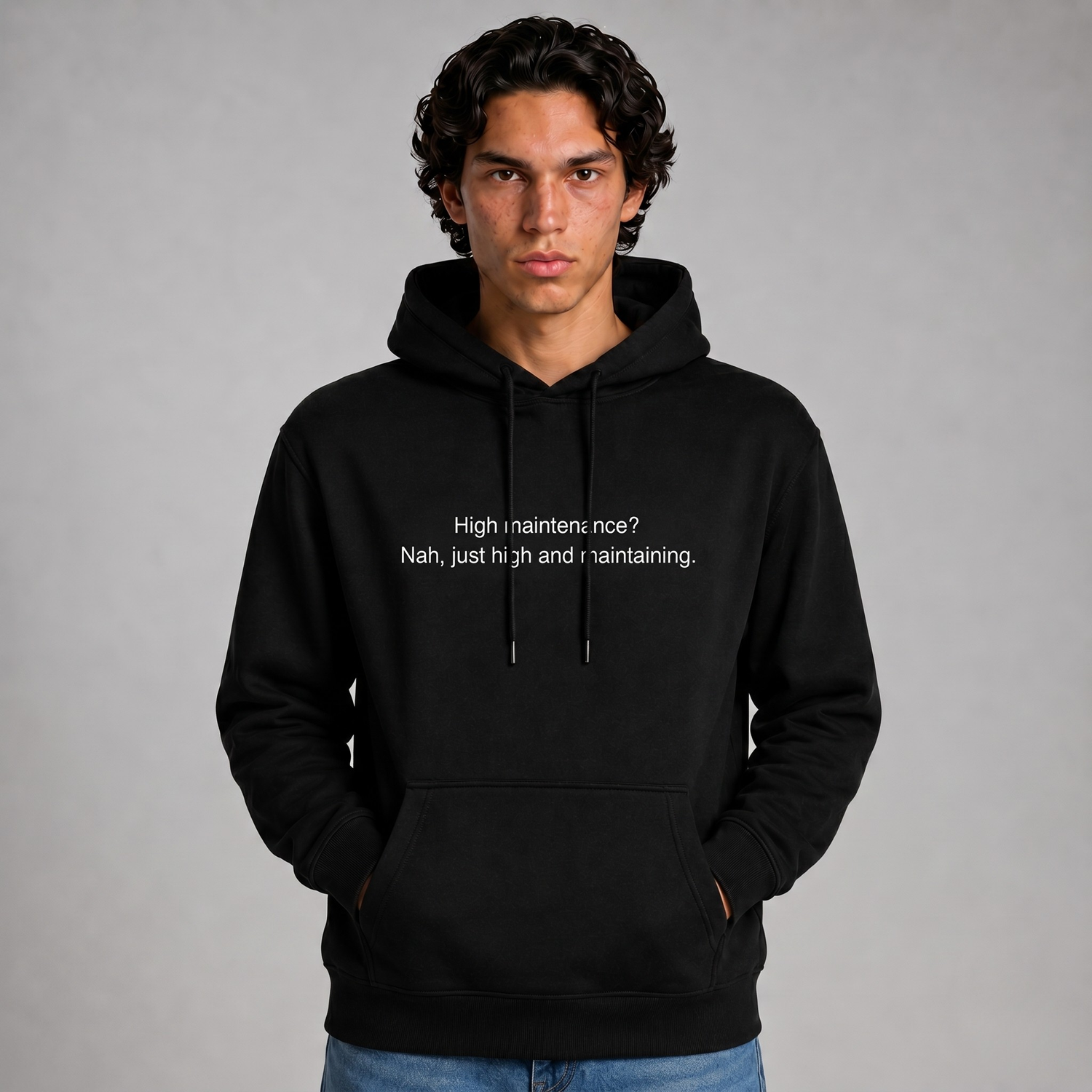 Person wearing a black thick hoodie with text 'High maintenance? Nah, just high and maintaining'  with 400 GSM premium streetwear hoodie for men and women and blue jeans on a gray background.