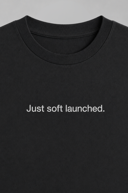 Black t-shirt with 'Just soft launched.' text on a gray background