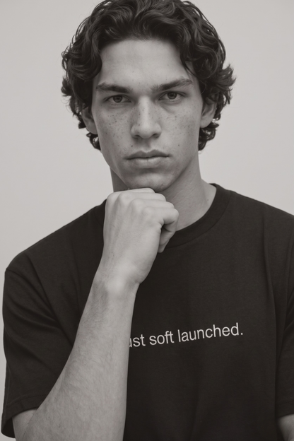 A close up shot of a person wearing a black t-shirt with text 'Just soft launched' with 240 GSM premium streetwear t-shirt for men and women.