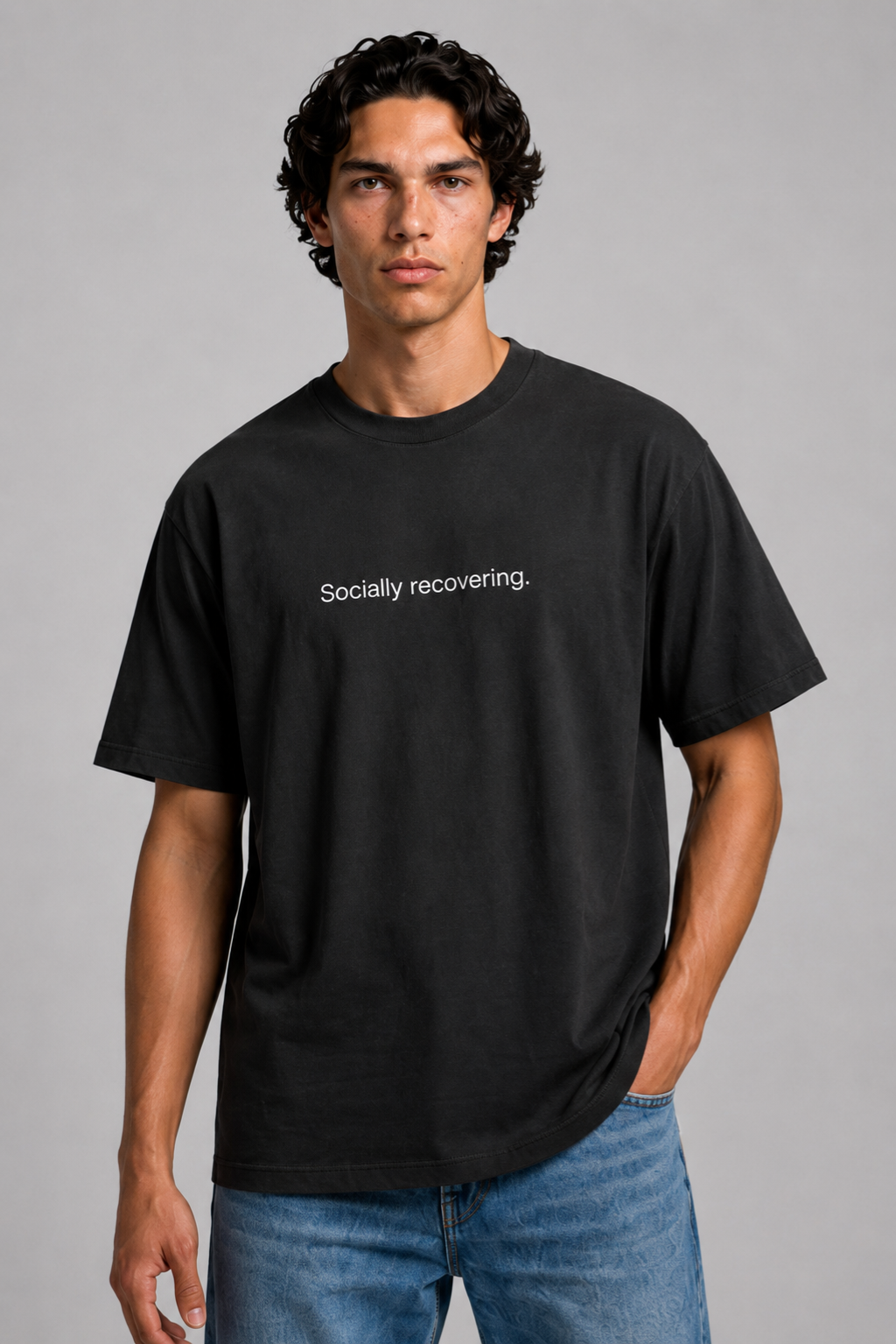 A close up shot of a person wearing a black t-shirt with text 'Socially recovering' with 240 GSM premium streetwear t-shirt for men and women and blue jeans on a gray background.